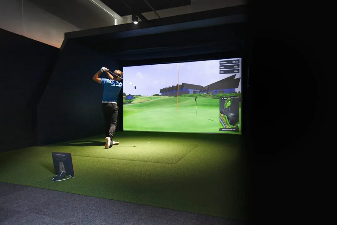 A player mid-swing inside a private, fully enclosed Swing Spot bay, a full course rendered on the wall-sized TrackMan screen.